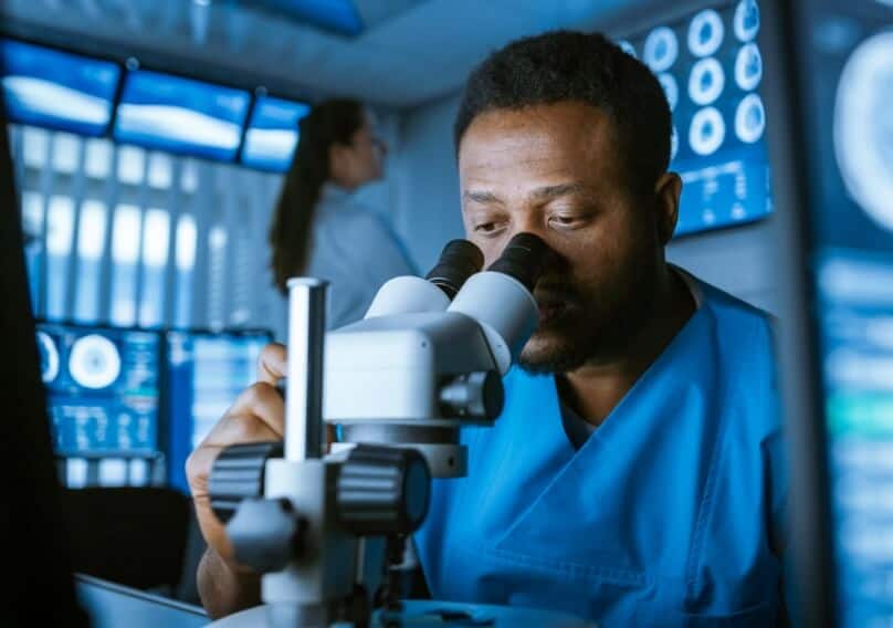 A person sits while studying something through a microscope