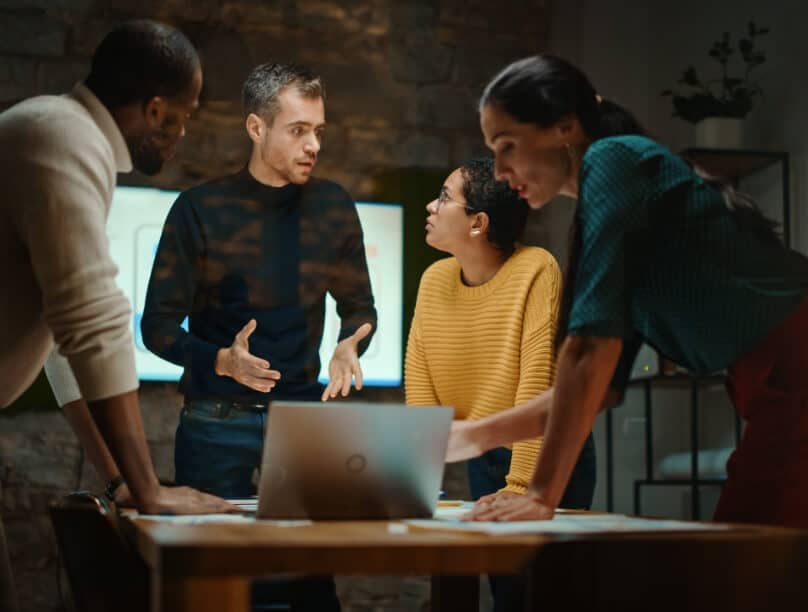 A group of people engage in a meeting around a table with a laptop computer on it